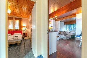 A modern hotel room with a wooden ceiling, a bed with red headboard, a sofa, a small table, and a window with curtains. - Villa Revita Kourouta Beach (Ilida)