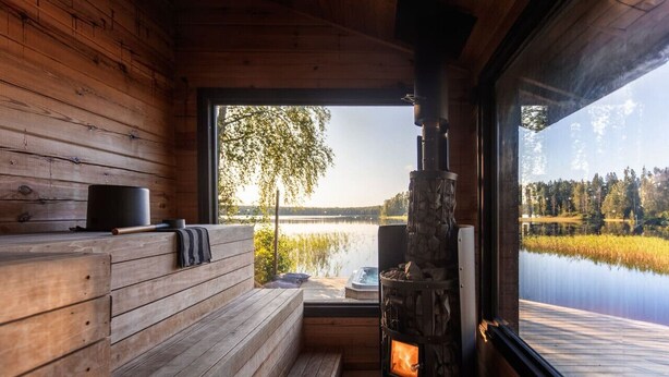 A wooden cabin interior with a stone fireplace, wooden benches, and a view of a lake. - Beautifully renovated red cottage by the lake (Salo)