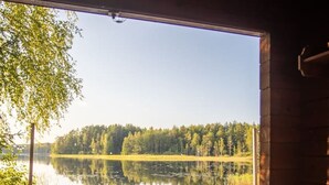A wooden deck with a hot tub and a boat docked on a calm lake, surrounded by trees. - Beautifully renovated red cottage by the lake (Salo)