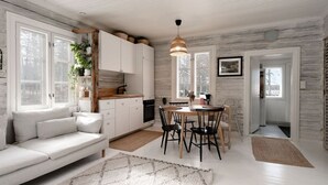 A modern kitchen with white cabinets, a dining table, and chairs. There is a sofa with cushions and a rug on the floor. - Beautifully renovated red cottage by the lake (Salo)