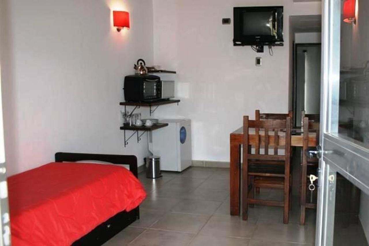 Habitació compacta amb llit, taula petita, cadira, microones, rentadora i televisió penjada a la paret.