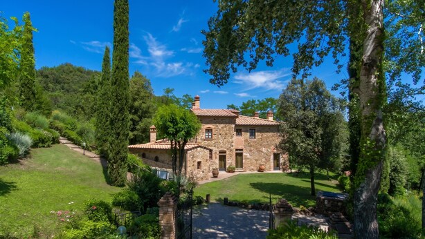 Une maison en pierre avec un toit de tuiles, entourée d’une végétation luxuriante et d’une pelouse bien entretenue.