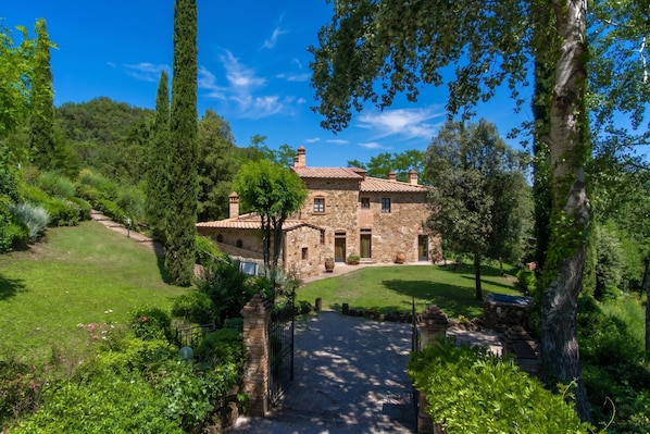 A stone house with a tiled roof, surrounded by lush greenery and a well-maintained lawn.