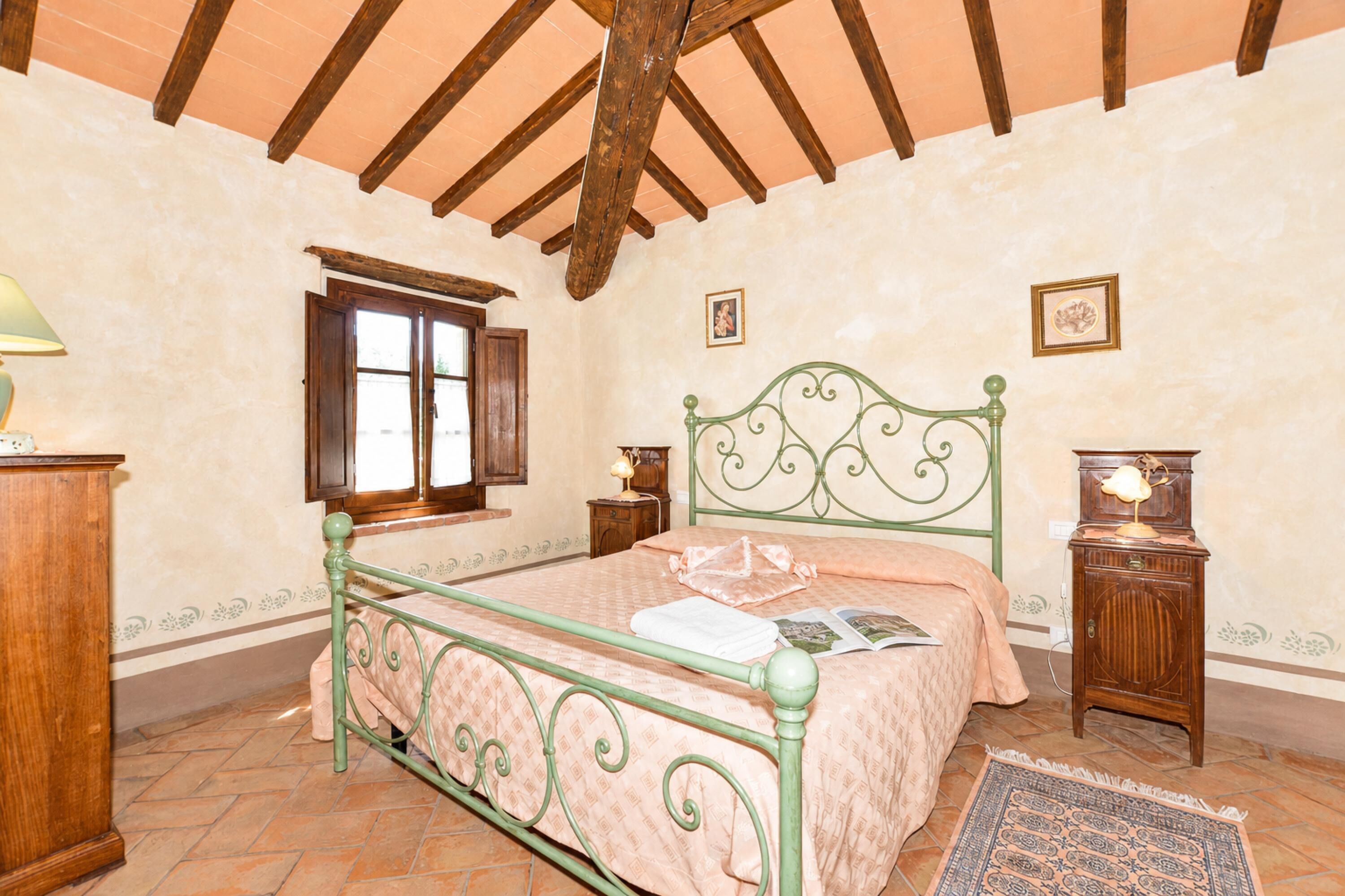 A bedroom with a bed, wooden headboard, a window, a nightstand, and a lamp.