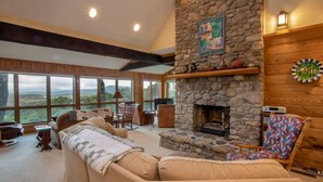 Un salón acogedor con chimenea de piedra, ventanas amplias que ofrecen vistas panorámicas y un mobiliario cómodo.