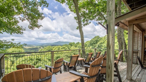 Una terraza de madera con sillas Adirondack y una vista panorámica de un paisaje montañoso.