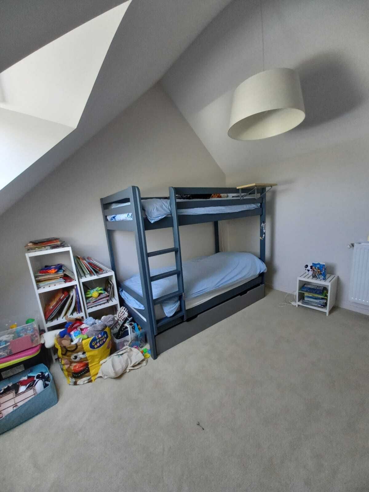 Une chambre de type dortoir, avec des lits superposés, une bibliothèque, une petite armoire blanche et un puits de lumière.