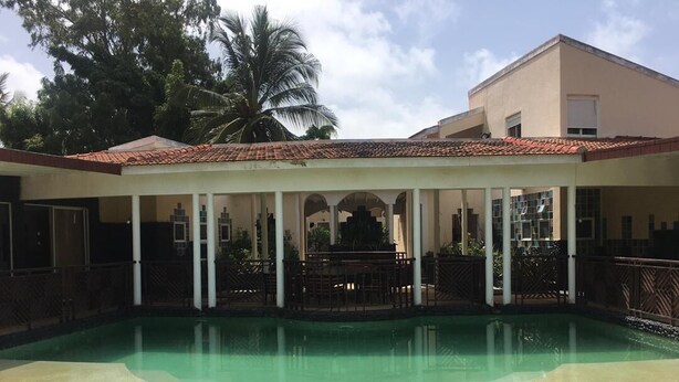 A covered swimming pool with a tiled roof, surrounded by a white fence and palm trees. - House (Saly)