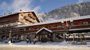 Un hôtel à la façade en bois, doté de nombreux balcons et dont l’entrée est recouverte de neige.