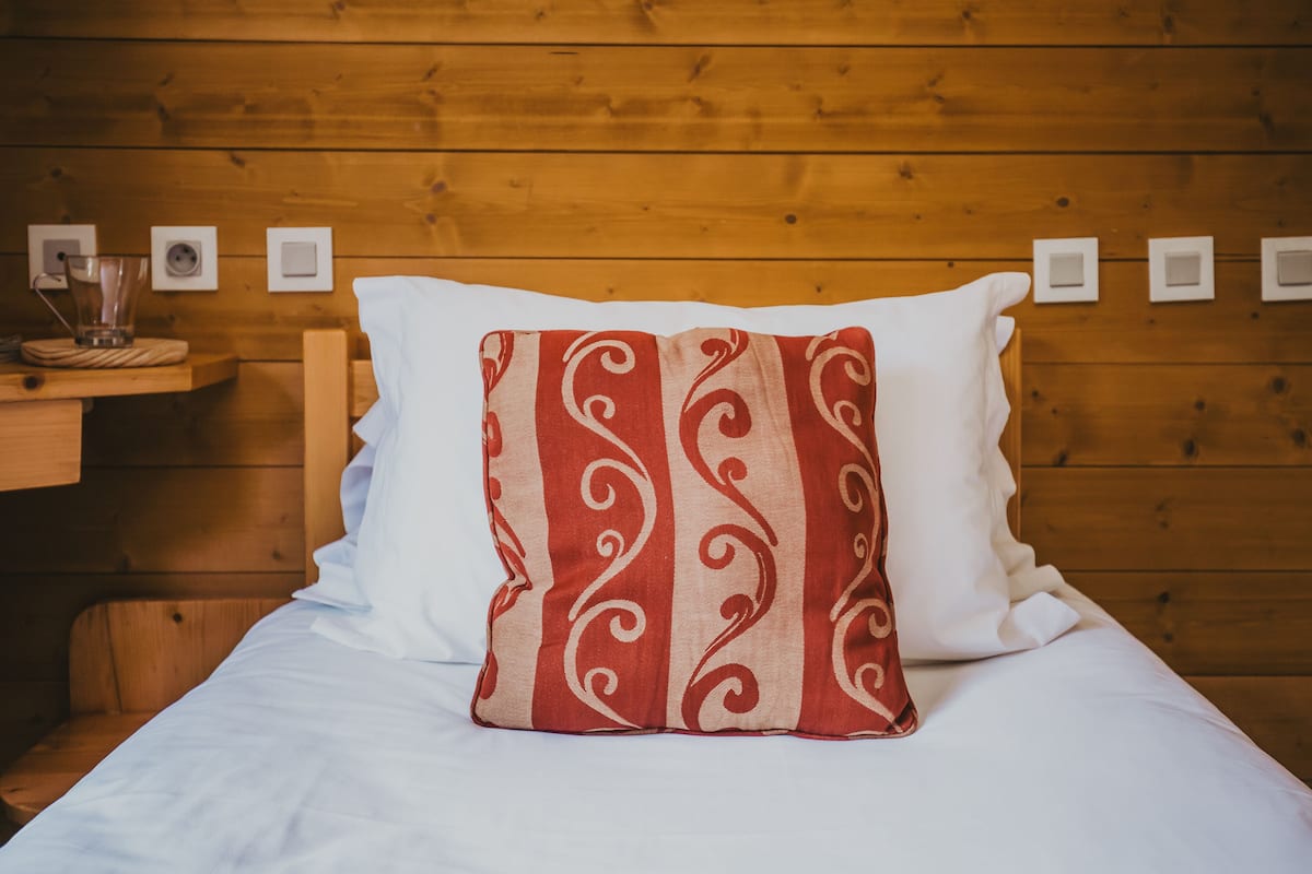 Una cama con un almohadón blanco y otro almohadón de diseño rojo y blanco.