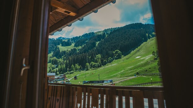 Un balcon en bois offrant une vue sur une colline verdoyante et un bâtiment situé au loin.