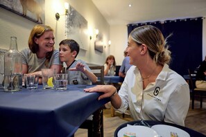 Eine Gruppe von Personen sitzt an einem Tisch mit verschiedenen Gläsern und Flaschen in einem Raum, der mit einer blauen Tischdecke und Wandleuchten ausgestattet ist.