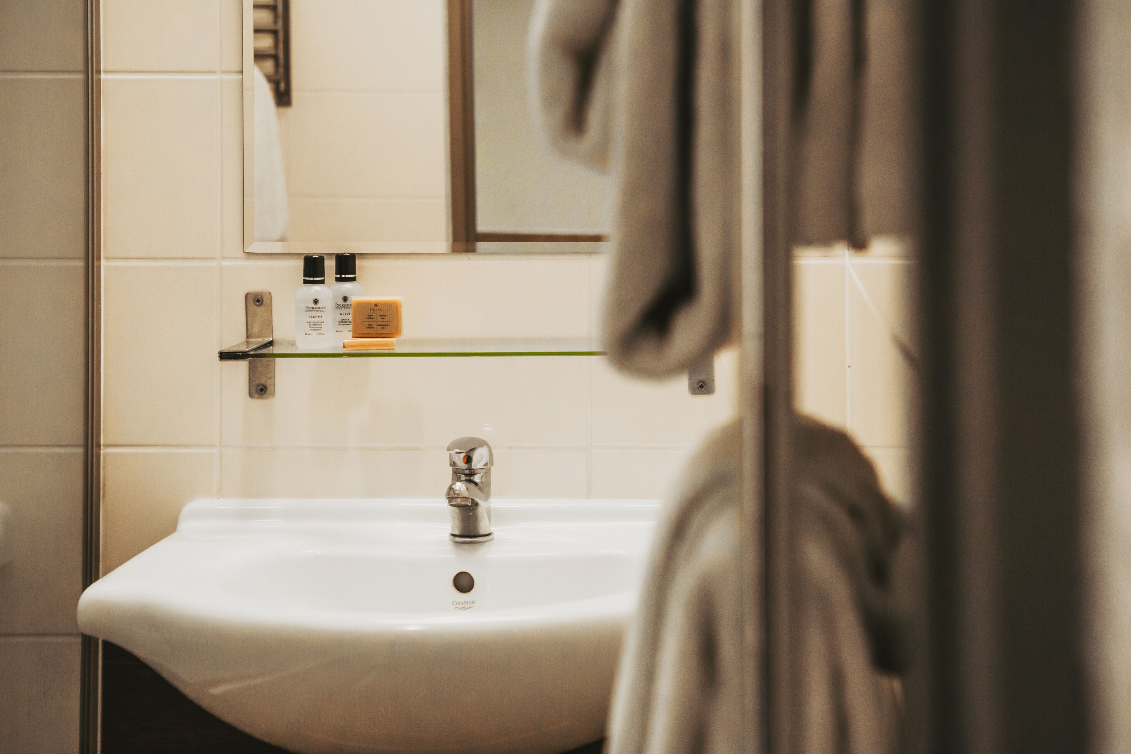 A bathroom with a white sink, a mirror, and a shelf with toiletries.