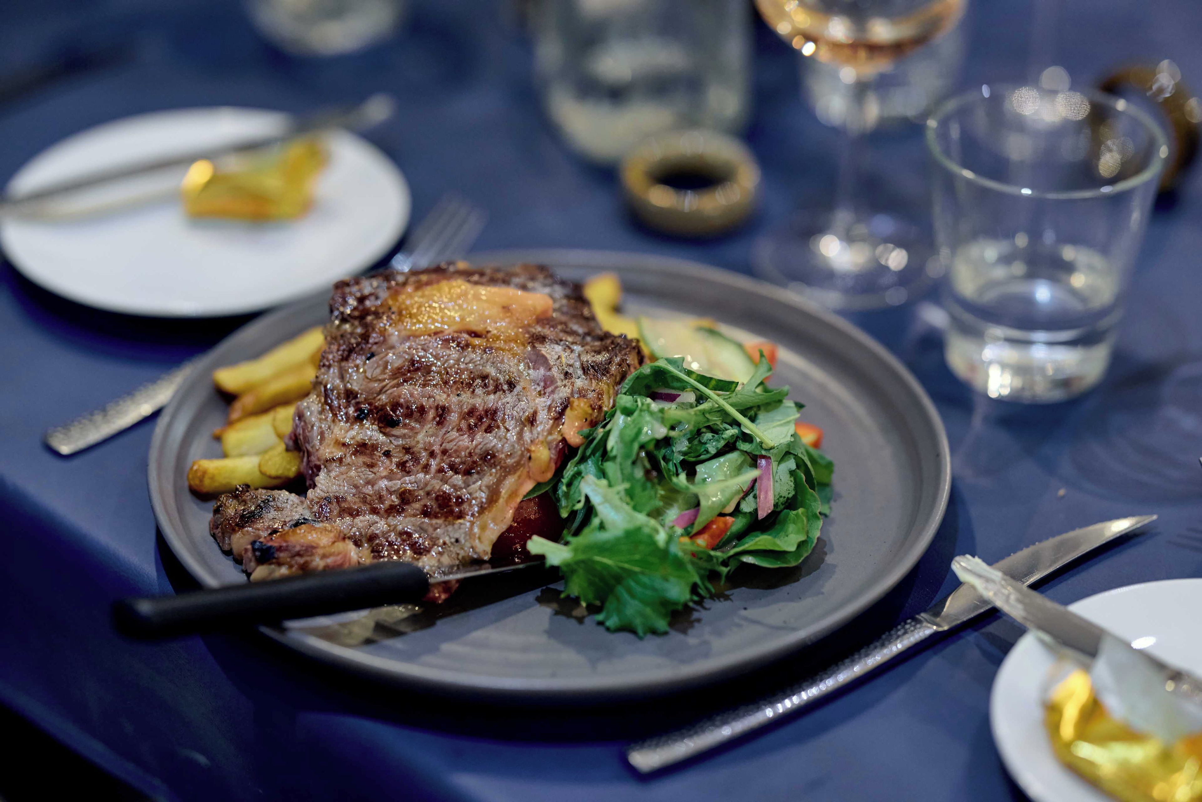 Ein Teller mit gegrilltem Fleisch, Pommes und Salat auf einem Tisch.