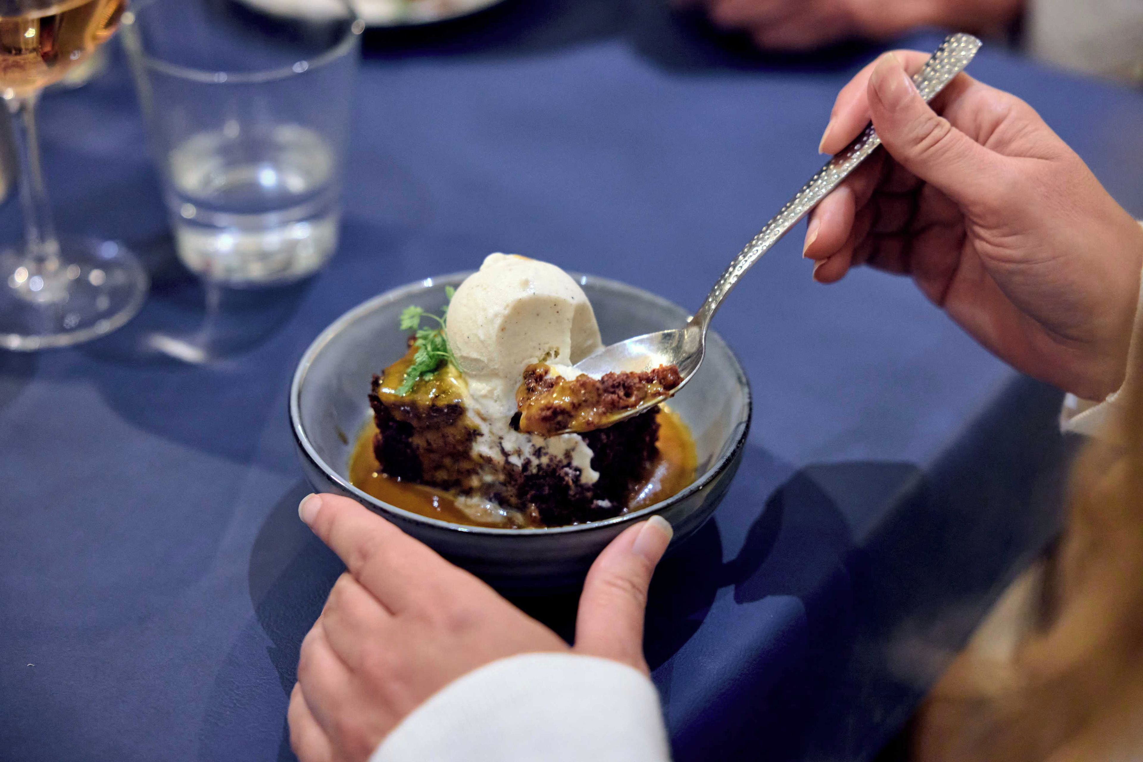 A dessert with ice cream and caramel sauce in a bowl, held by a person.