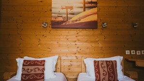 Une chambre rustique en bois avec deux lits, une tête de lit en bois et un tableau représentant un télésiège accroché au mur.