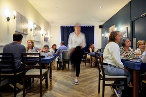 L’intérieur d’un restaurant, avec un plancher en bois, des tables, des chaises et des luminaires fixés aux murs.