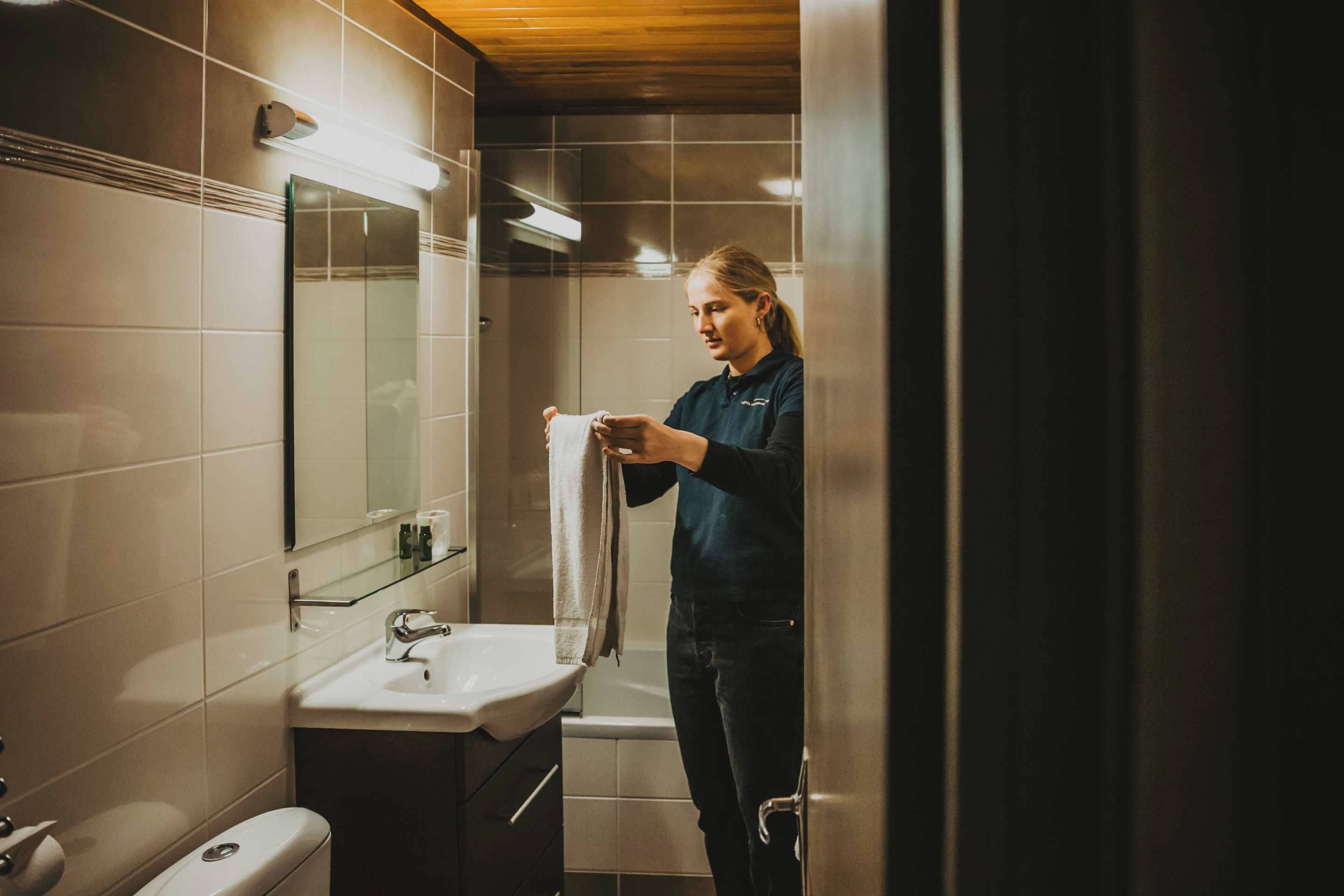 A person standing in a bathroom with a sink, mirror, and towel rack.