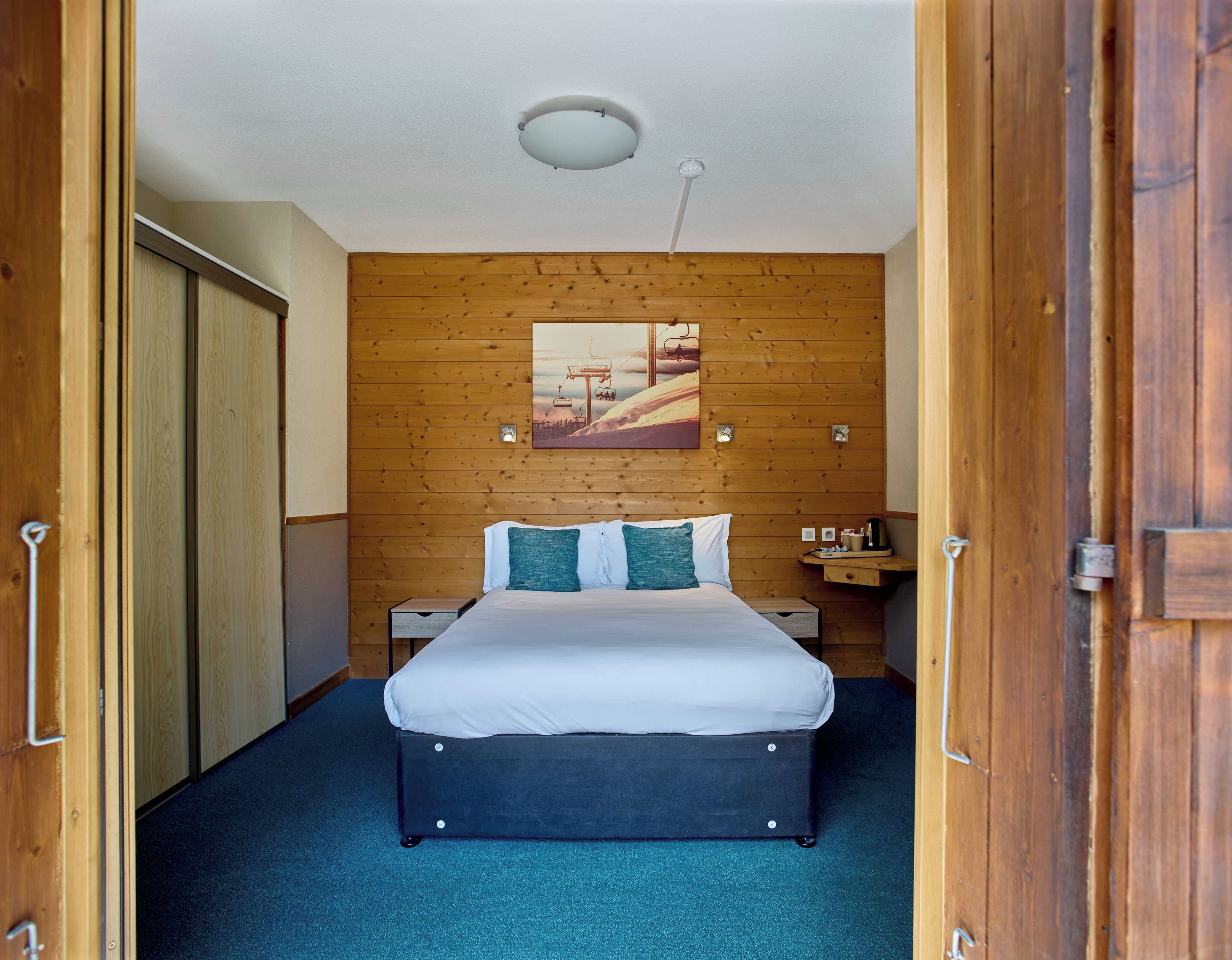 Una habitación de hotel con una cama, pared de madera, un cuadro y una lámpara de techo.