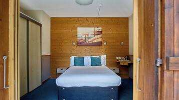 Una habitación de hotel con una cama, pared de madera, un cuadro y una lámpara de techo.