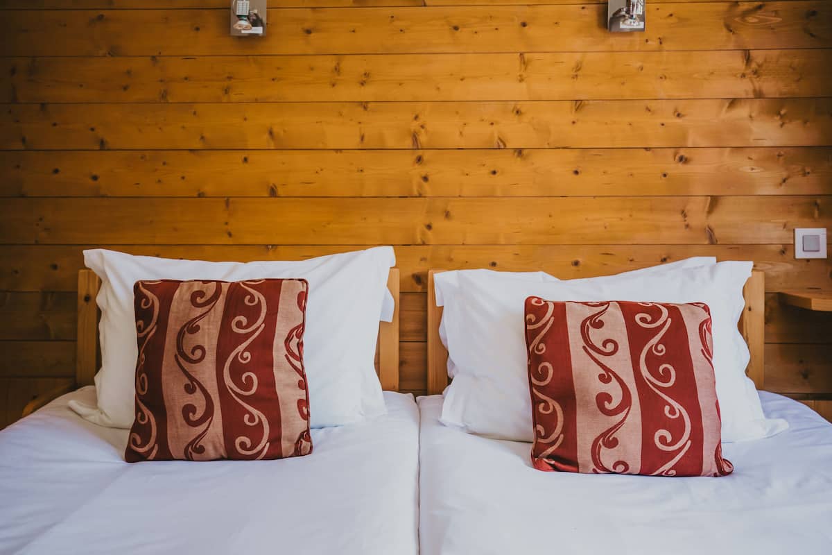 Una cama doble con ropa de cama blanca y dos almohadas decorativas con un diseño de remolino.