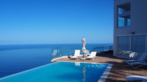 Una piscina azul cristalina con sillas de descanso y sombrillas, con vista al océano.