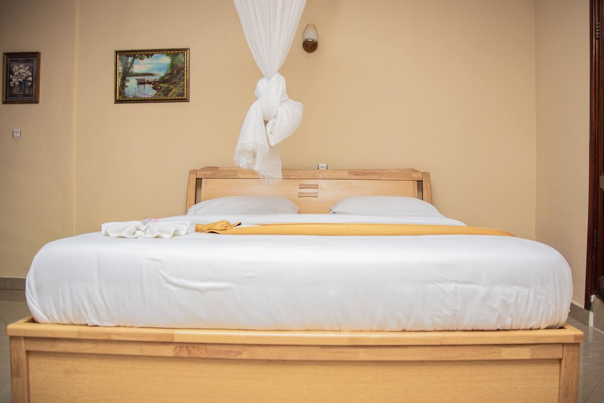 Uma cama bem arrumada com lençóis brancos, cabeceira de madeira e dossel.
