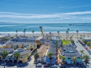Une ville côtière avec une jetée qui s’avance dans l’océan, une plage où se trouvent des gens et un parking rempli de voitures.