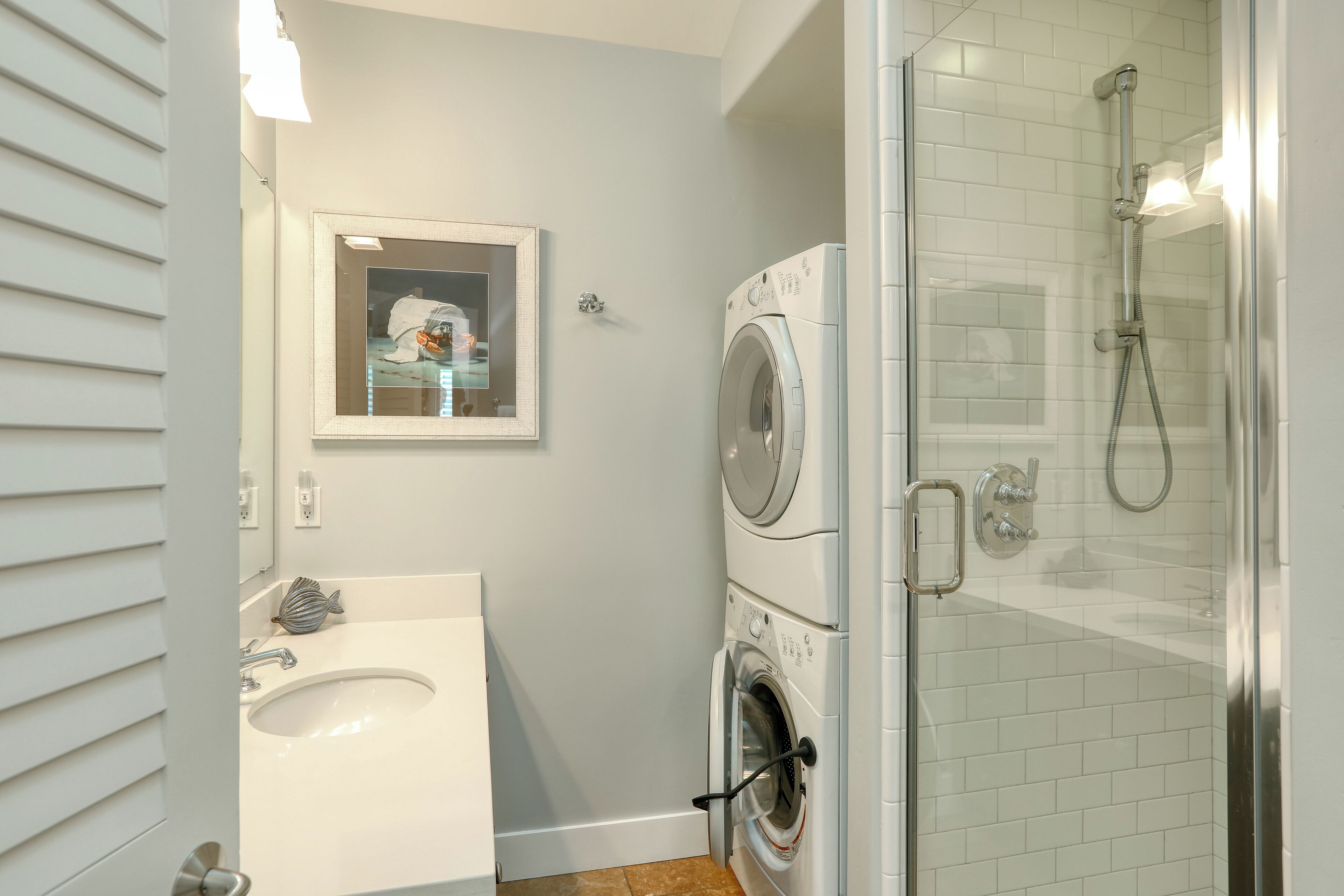 Une salle de bain moderne équipée d’un lavabo, d’un miroir, d’un lave-linge et d’une douche à parois de verre.