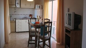 Une cuisine compacte avec des meubles blancs, un four à micro-ondes et un coin repas comprenant deux chaises en bois et une table.