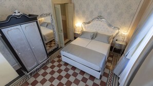 Une chambre avec un sol à carreaux, un lit doté d’une tête de lit blanche, un miroir et une armoire.