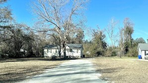 A single-story house with a front porch, surrounded by trees and a clear sky. - Quiet & Downtown Smart TVs in all bedrooms, minutes from base. (Havelock)