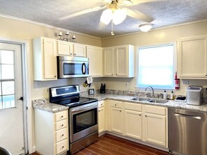 A kitchen with white cabinets, stainless steel appliances, a granite countertop, and a ceiling fan.