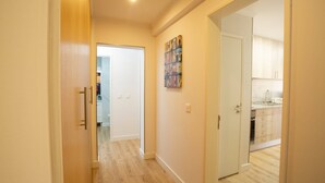 A hallway with wooden flooring, a door leading to a kitchen, and a colorful artwork on the wall. - Meriteluna Pateo - beetwen Lisboa Sintra e Cascais (Agualva-Cacém)