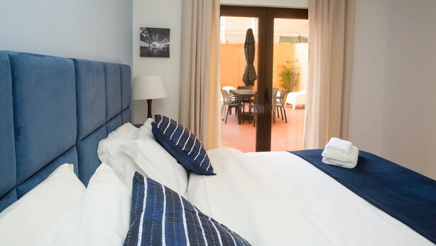 A hotel room with a large bed, a headboard, a bedside table with a lamp, and a view of an outdoor patio with chairs and a table. - Meriteluna Pateo - beetwen Lisboa Sintra e Cascais (Agualva-Cacém)