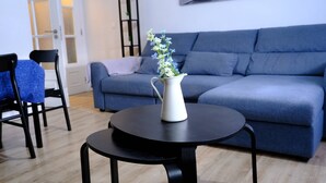 A modern living room with a blue sofa, a small round table with a white vase, and a dining area with chairs. - Meriteluna Pateo - beetwen Lisboa Sintra e Cascais (Agualva-Cacém)