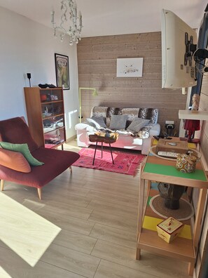 A living room with a sofa, a red armchair, a wooden floor, a chandelier, and a wall-mounted air conditioner.