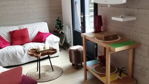 Een gezellige woonkamer met een witte bank, rode kussens, een houten salontafel en een televisie op een witte dressoir.