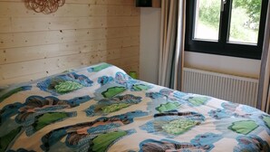 Een slaapkamer met een houten wand, een bed met een beddengoed met patroon, een spiegel en een raam met gordijnen.
