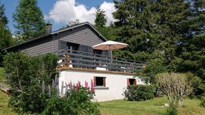 Een huis met twee verdiepingen, een grijs dak, een balkon en een tuin met paarse bloemen.