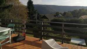 Een balkon met uitzicht op een bergachtig landschap, een tafel, stoelen en een klein wit tafeltje.