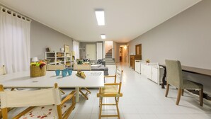 Tilava ruokailutila, jossa on pitkä pöytä, puiset tuolit ja tarjoilupöytä, jossa on hedelmiä ja juomia.