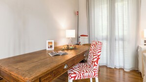 Ruokailutilassa on puinen pöytä, punavalkoinen kuviollinen tuoli, lamppu ja ikkuna, jossa on läpikuultavat verhot.