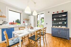 A modern kitchen with a dining table set for four, wooden chairs, a blue dishwasher, and a blue cabinet with shelves above. - Villa Paola Tremezzo (Tremezzina)