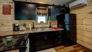A compact kitchen with dark cabinets, a black refrigerator, a stove, and a sink. - Dragon's Nest Mountain View (Robbinsville)