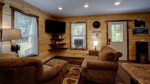 A cozy cabin interior with wooden walls, a television mounted on the wall, a fireplace, and a rug with animal prints. - Dragon's Nest Mountain View (Robbinsville)