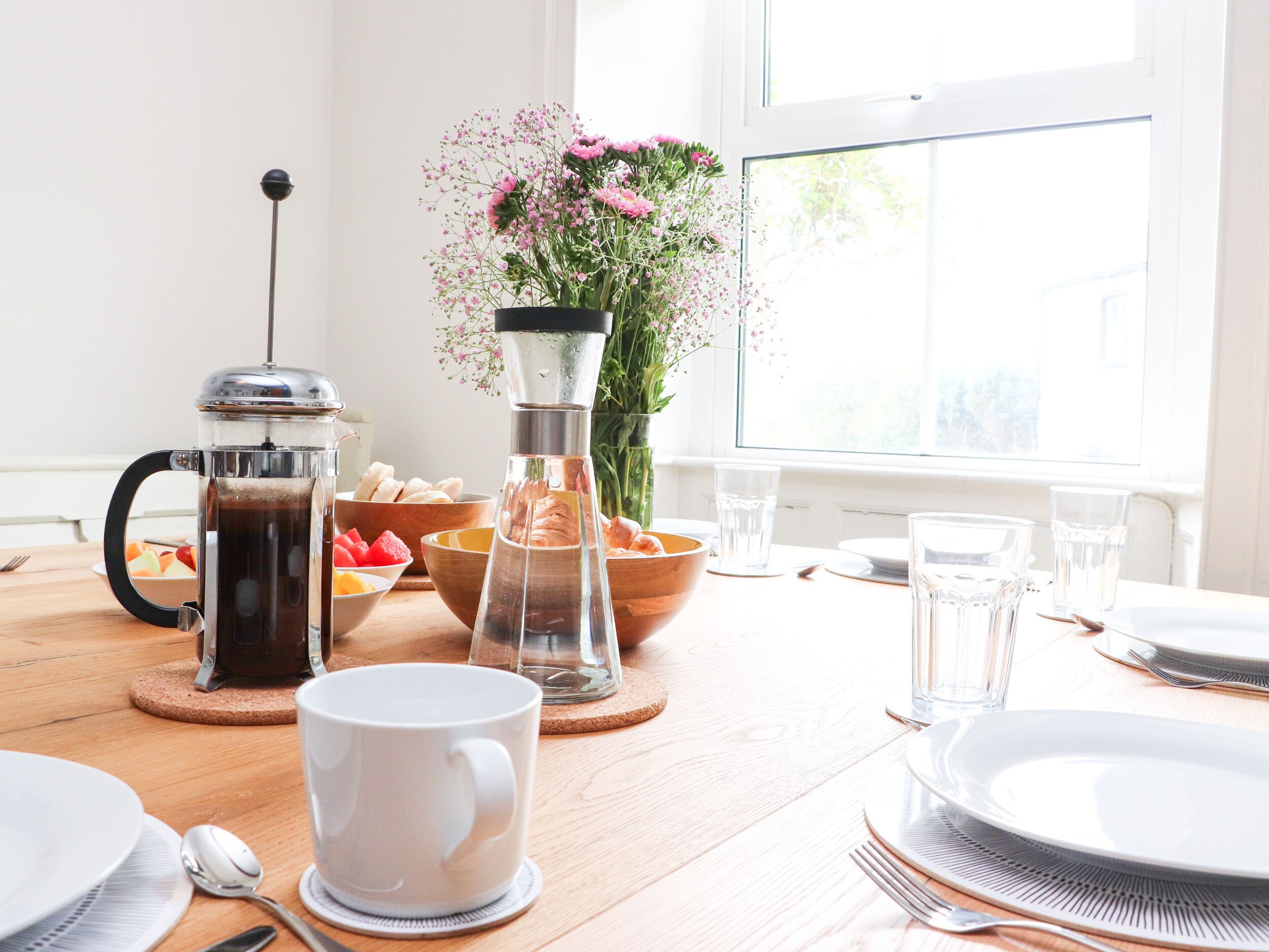 Ein Esstisch mit Kaffeemaschine, Obstschalen und einem Blumenstrauß.