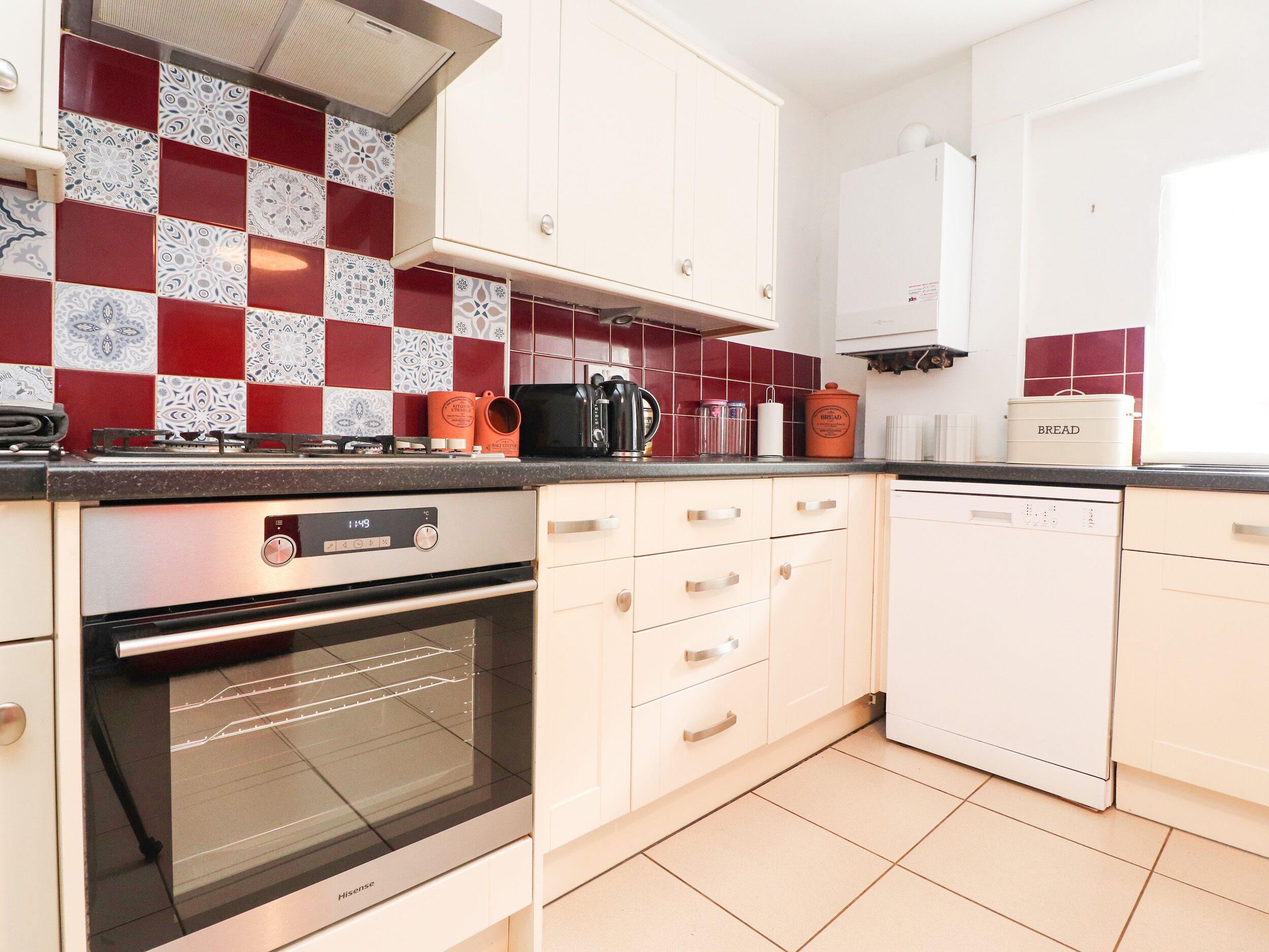A kitchen with a gas stove, oven, and dishwasher, white cabinets, and red and white patterned backsplash tiles.