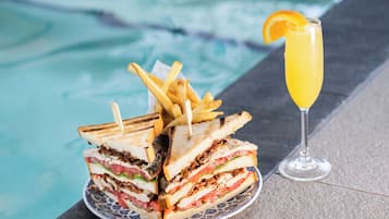 Une assiette de sandwichs grillés et de frites, à côté d’un verre de jus d’orange, près d’une piscine.