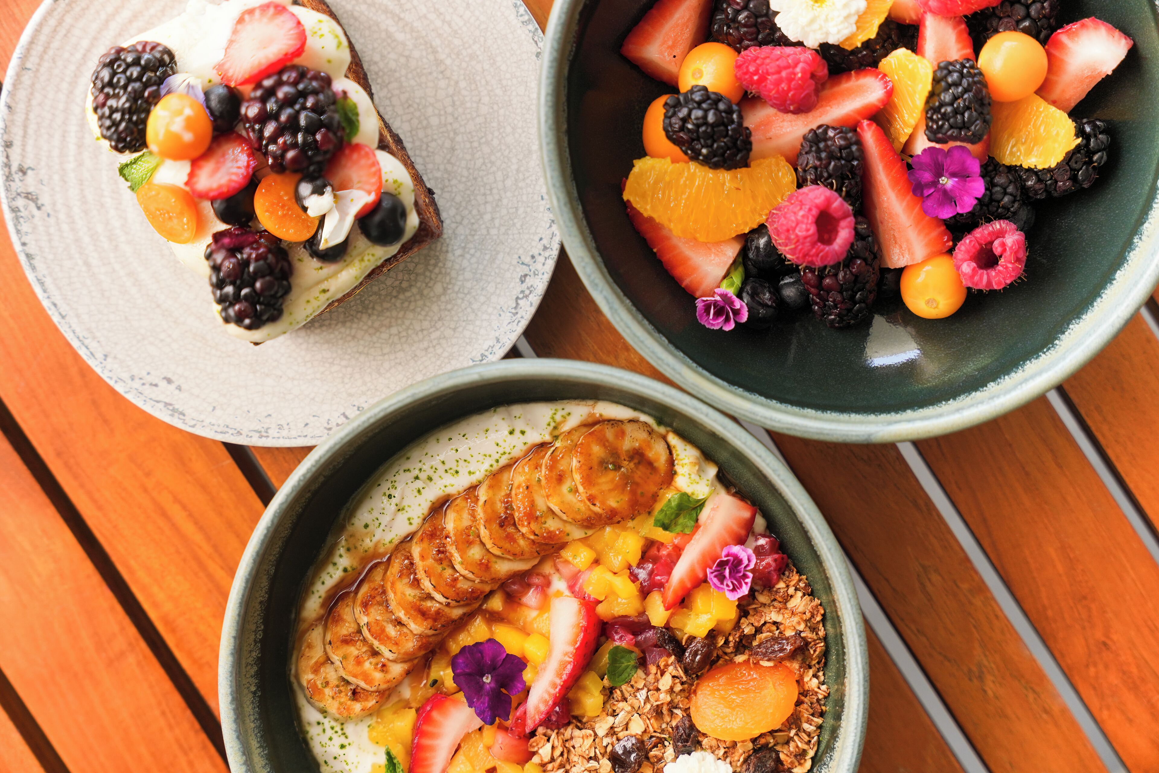 Tres tazones de ensalada de frutas con diversas bayas y frutas.